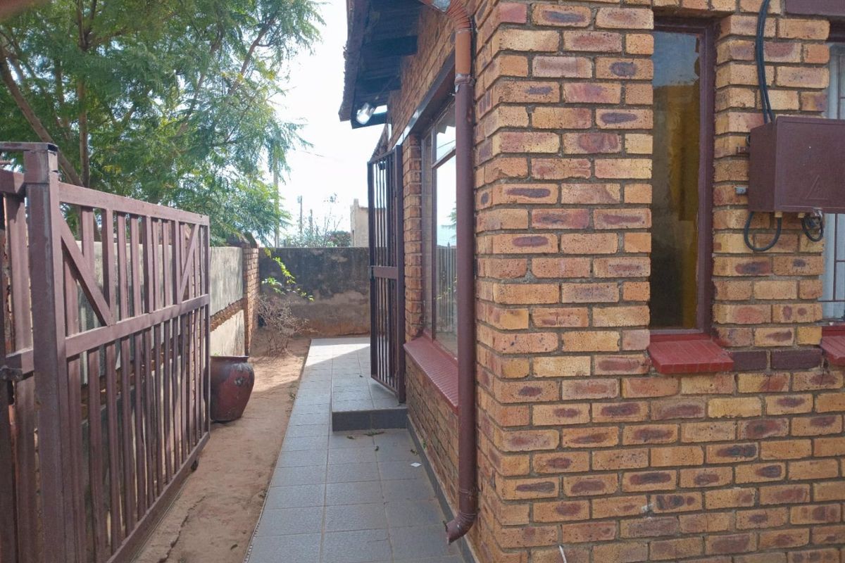 Side exterior view of the property featuring face brick walls, a tiled walkway, and metal security gate access.
