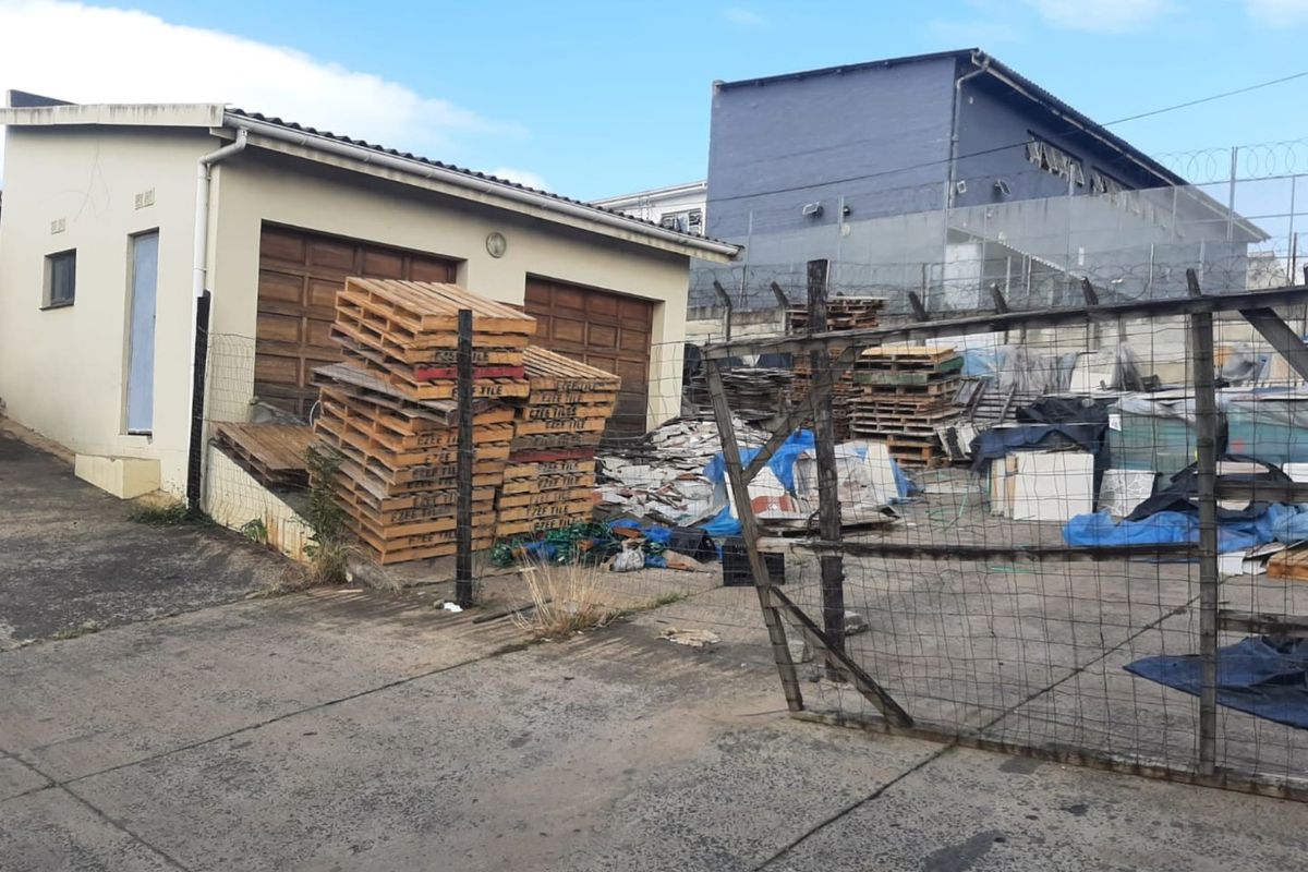 Rear exterior yard area featuring concrete paving, security fencing with razor wire, and access to garage doors.