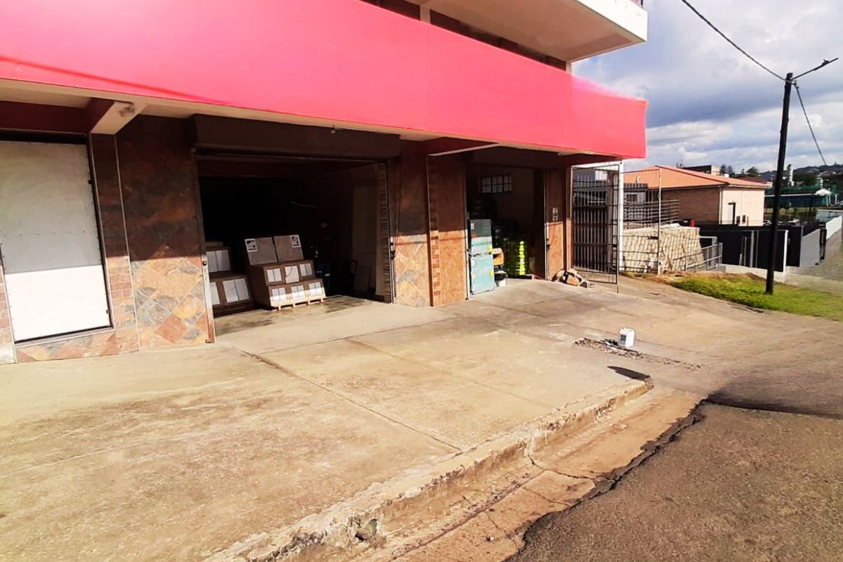 Commercial property frontage featuring a concrete driveway, tiled facade, and large roller shutter doors with a prominent red signage fascia.