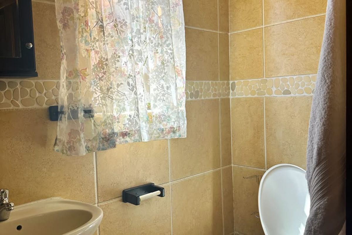 A compact bathroom featuring a pedestal basin, toilet, and neutral ceramic wall and floor tiling with a decorative border.