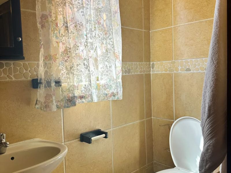 A compact bathroom featuring a pedestal basin, toilet, and neutral ceramic wall and floor tiling with a decorative border.