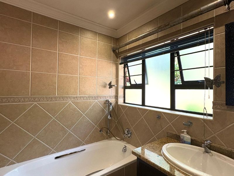 A functional bathroom featuring a built-in bathtub, vanity cabinet with granite countertop, and tiled finishes throughout.