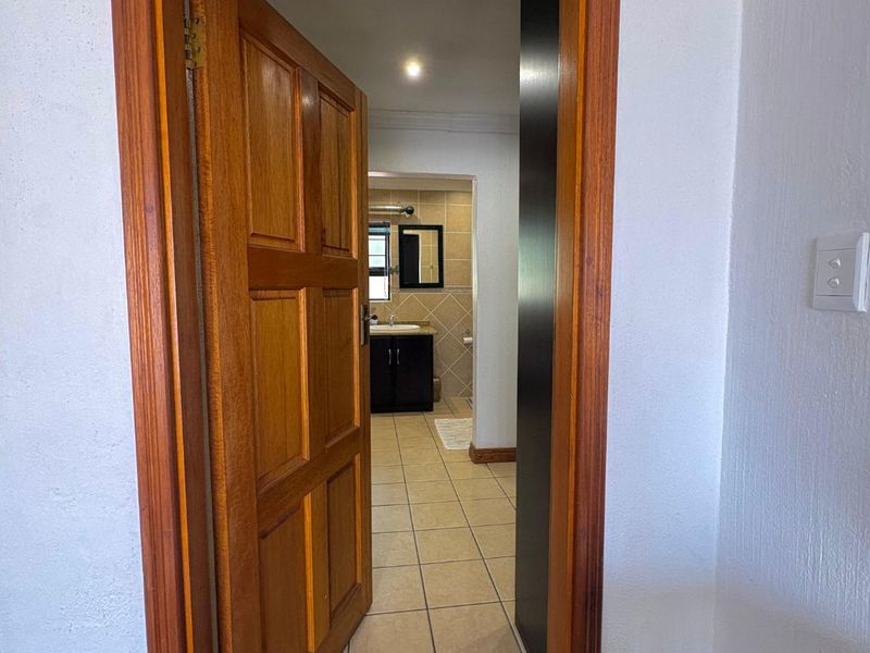 A view through a wooden door frame into a tiled bathroom area featuring a vanity and mirror.