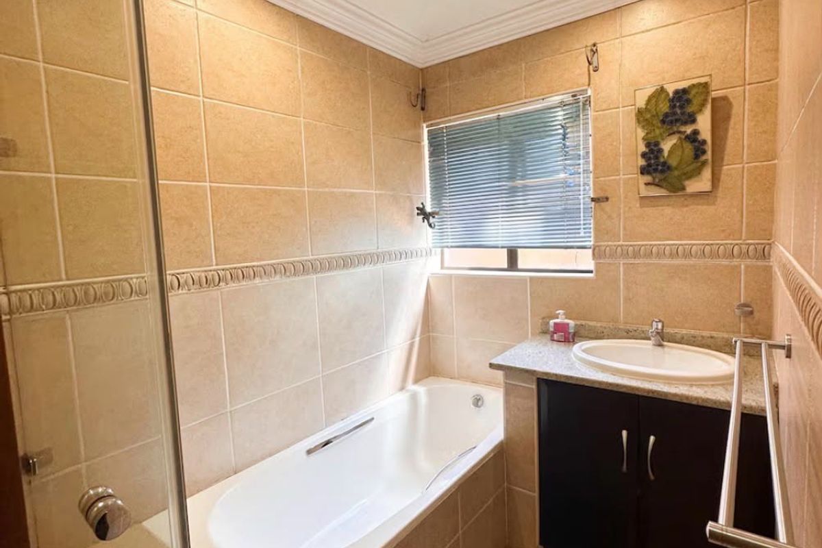 A functional bathroom featuring a built-in vanity, a drop-in bathtub with a glass shower screen, and neutral wall tiling.