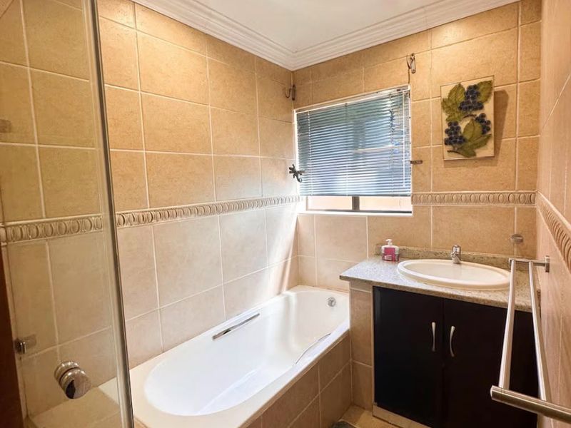 A functional bathroom featuring a built-in vanity, a drop-in bathtub with a glass shower screen, and neutral wall tiling.