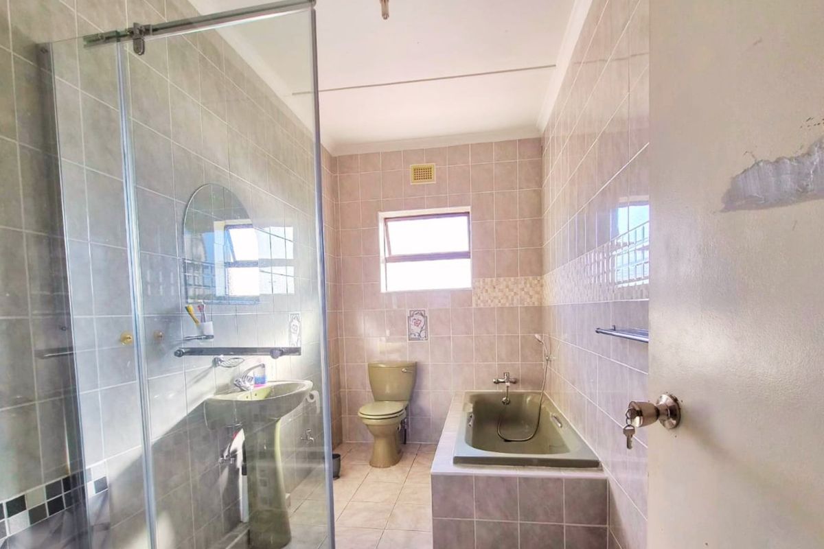 A functional bathroom featuring a built-in bathtub, glass shower enclosure, pedestal basin, and toilet with neutral wall and floor tiling.