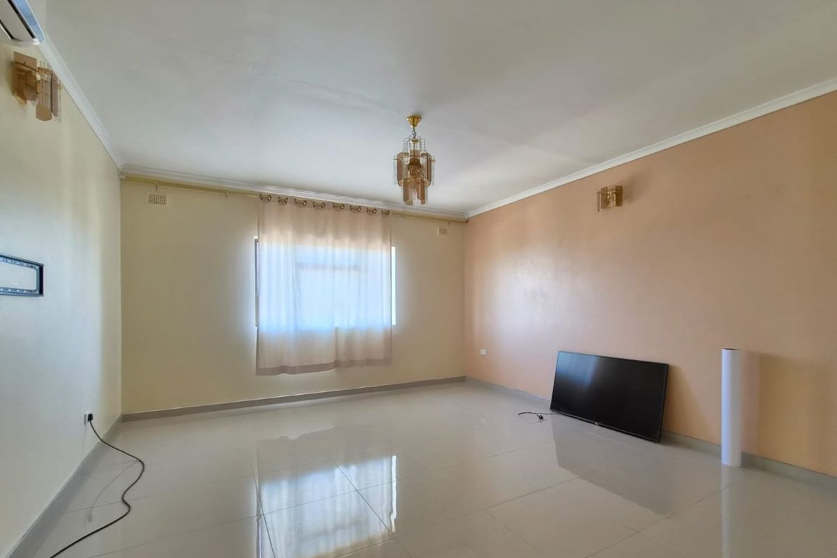 A spacious, empty living room featuring tiled flooring, neutral wall tones, ceiling coving, and integrated lighting fixtures.