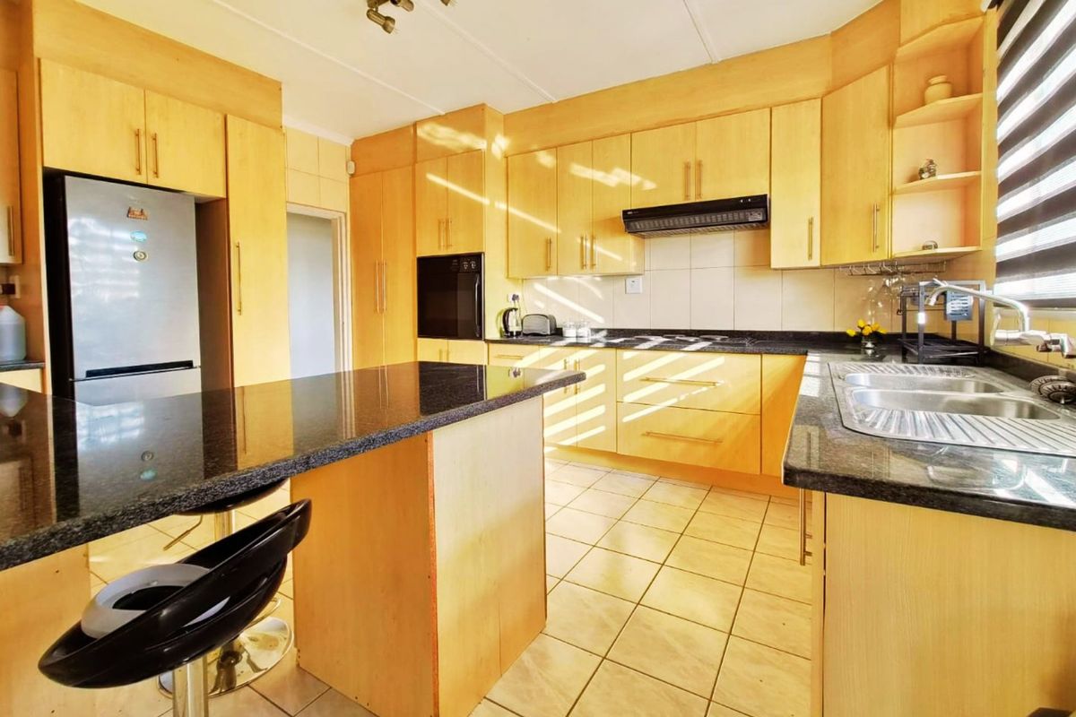 A functional kitchen featuring light wood cabinetry, dark granite countertops, a built-in oven, extractor fan, and tiled flooring.