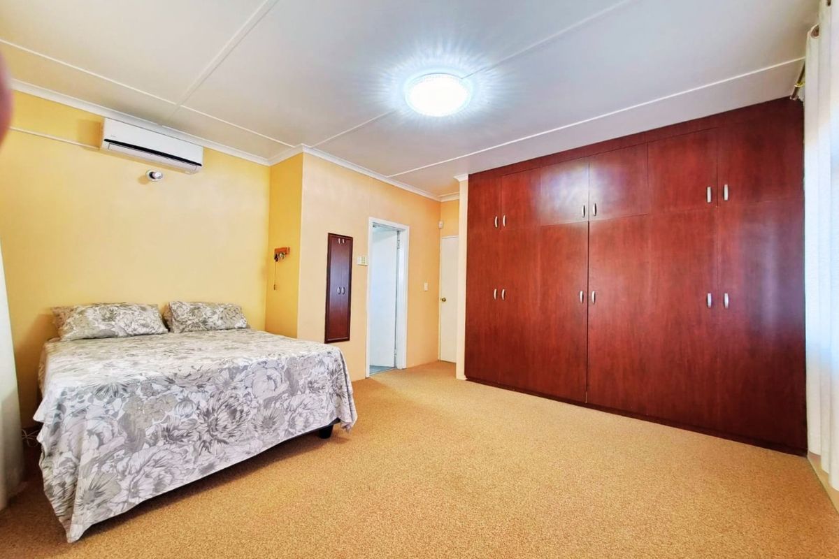 Spacious bedroom featuring extensive built-in wooden cabinetry, carpeted flooring, and a wall-mounted split-system air conditioning unit.