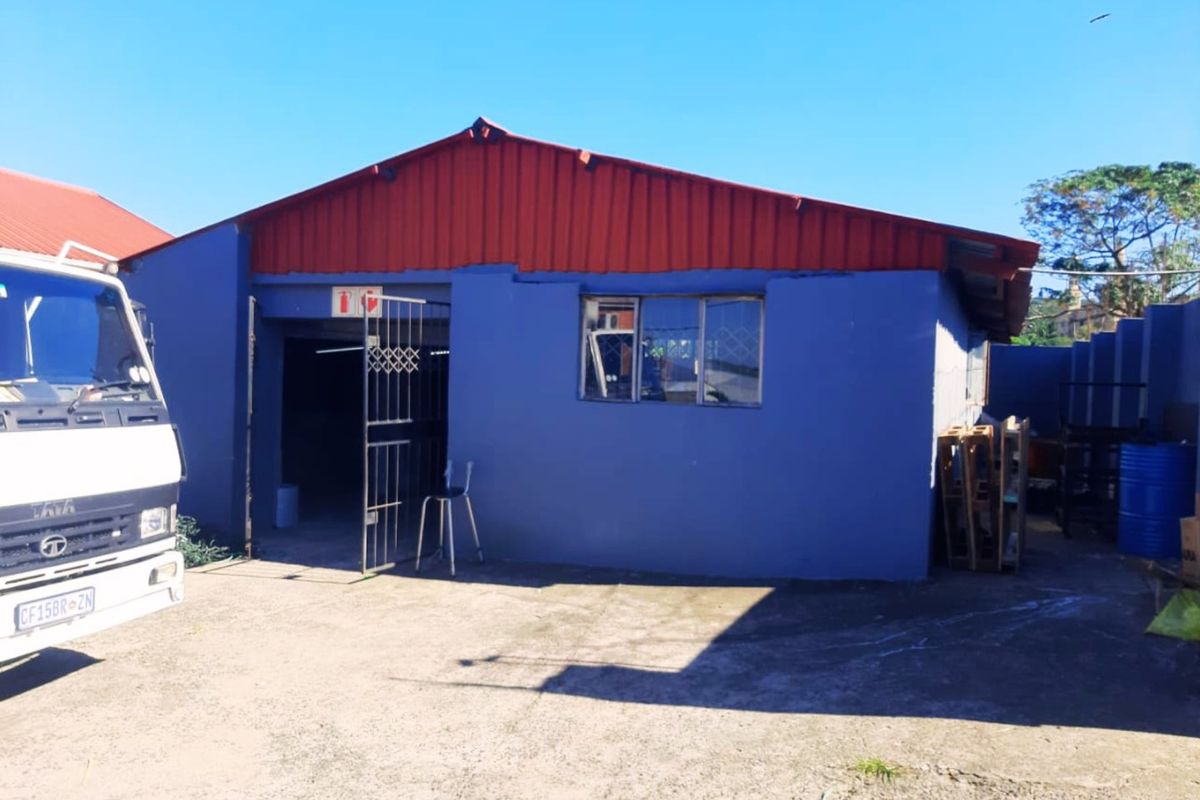 Front view of an industrial building featuring a corrugated metal roof, blue painted exterior walls, and a concrete driveway.