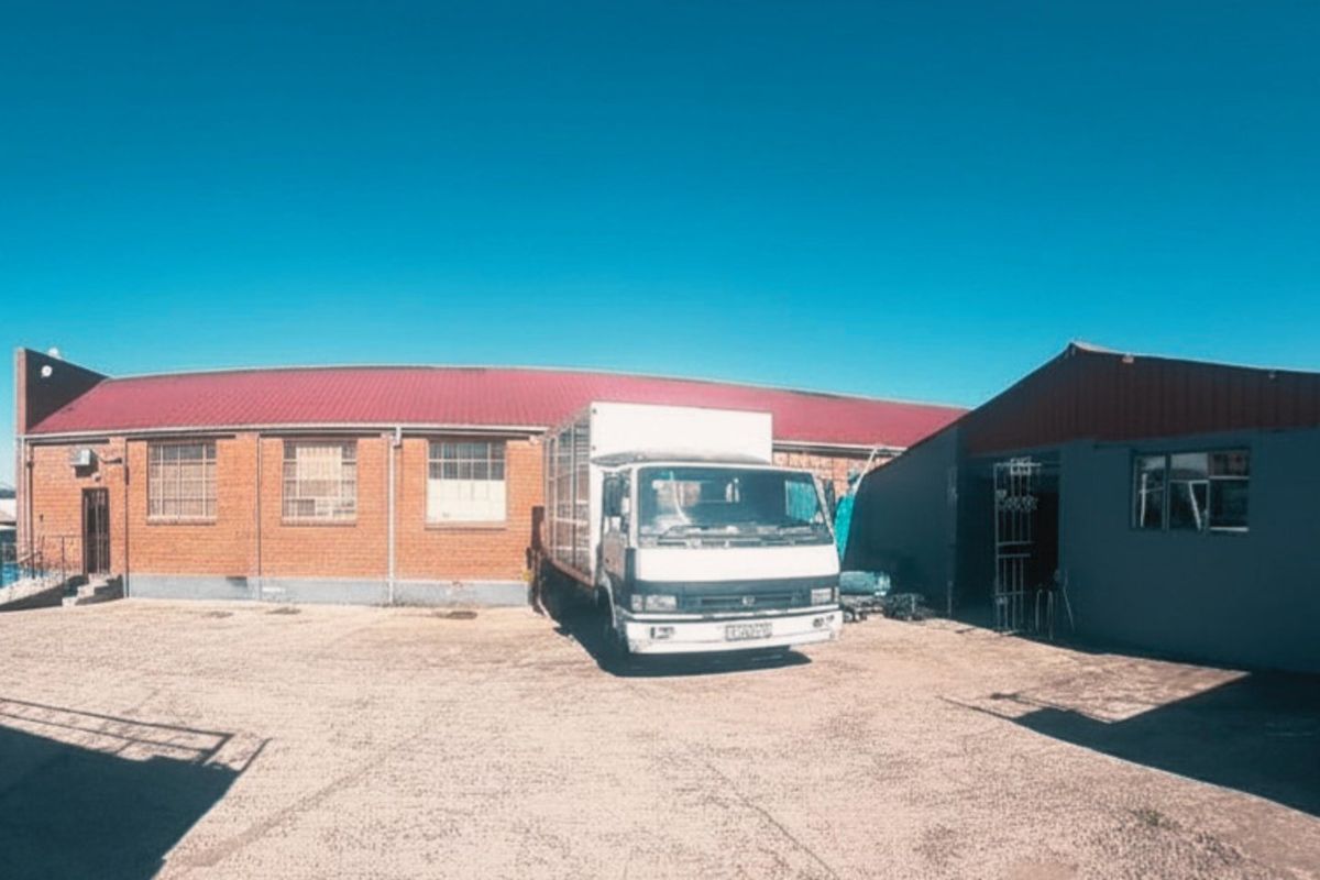 Industrial property exterior featuring a brick facade, corrugated metal roofing, and a large concrete yard area suitable for logistics or storage.