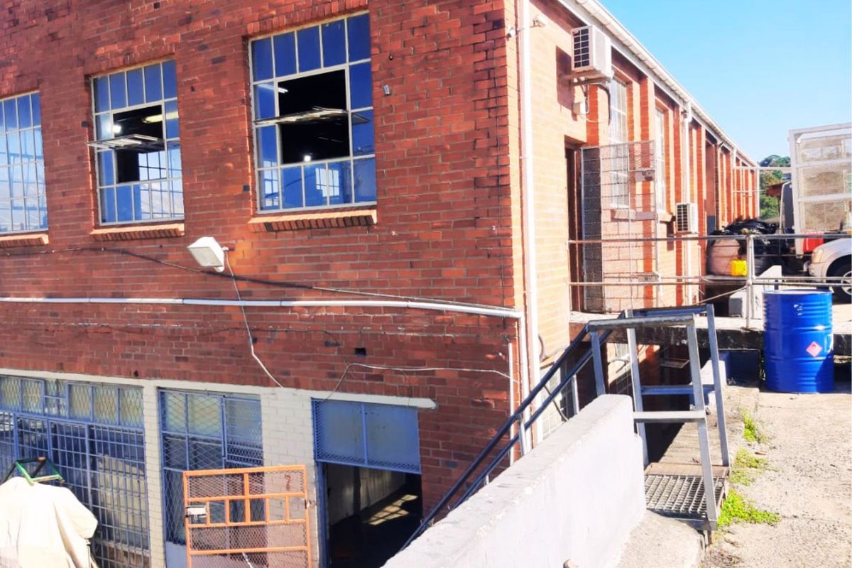 Rear exterior view of an industrial brick building featuring steel-framed windows, an external staircase, and a concrete loading area.