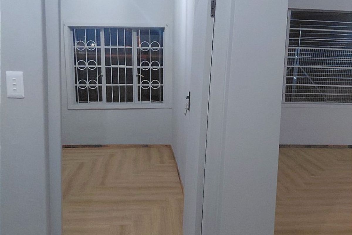 An empty bedroom featuring light-toned laminate flooring and security bars on the windows, presenting a clean, neutral space ready for personalization.