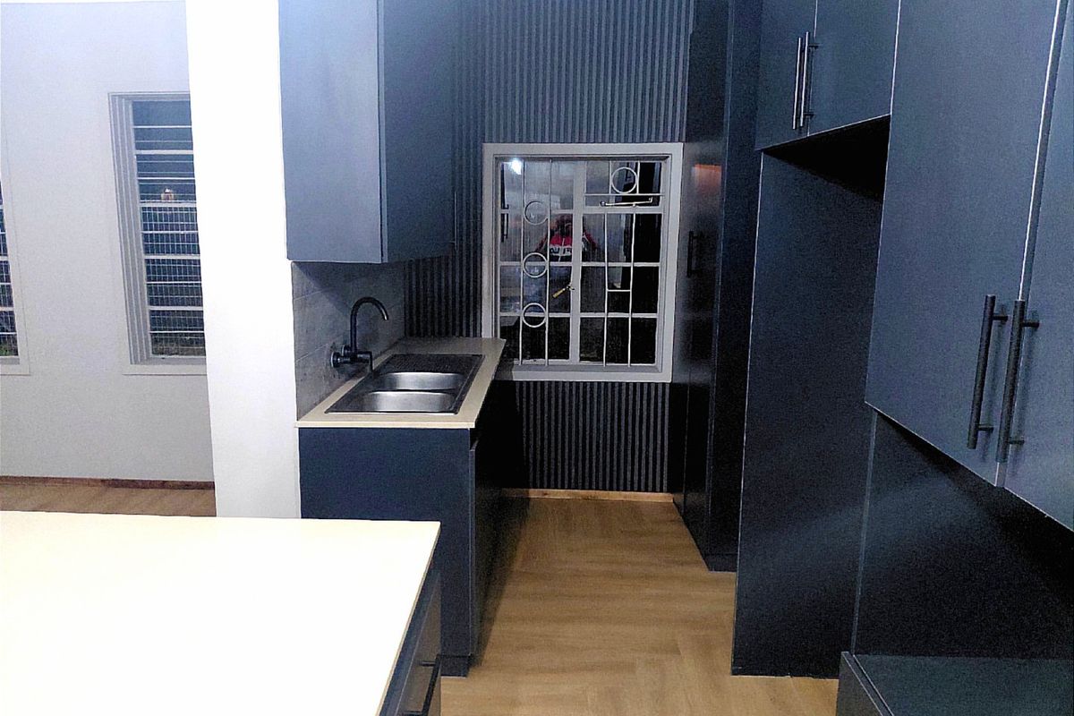 Modern kitchen featuring dark cabinetry, double sink with matte black tap, and light wood-look flooring in a clean, contemporary space.