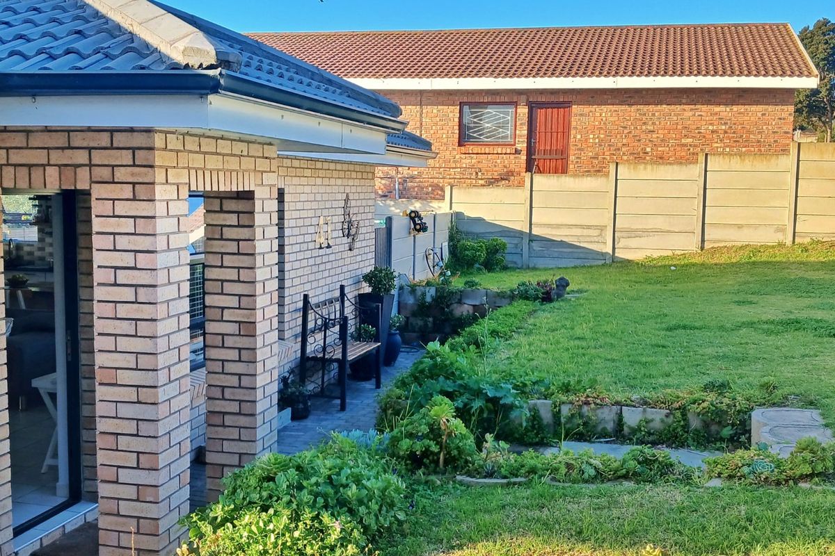 A view of the rear exterior featuring a brick-built home, a paved patio area, and a well-maintained garden with a precast concrete boundary wall.