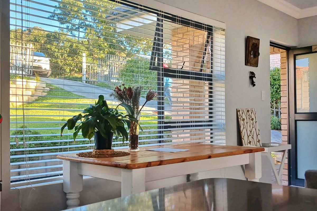 A bright living area featuring large windows with venetian blinds, providing natural light and views of the front garden and driveway.