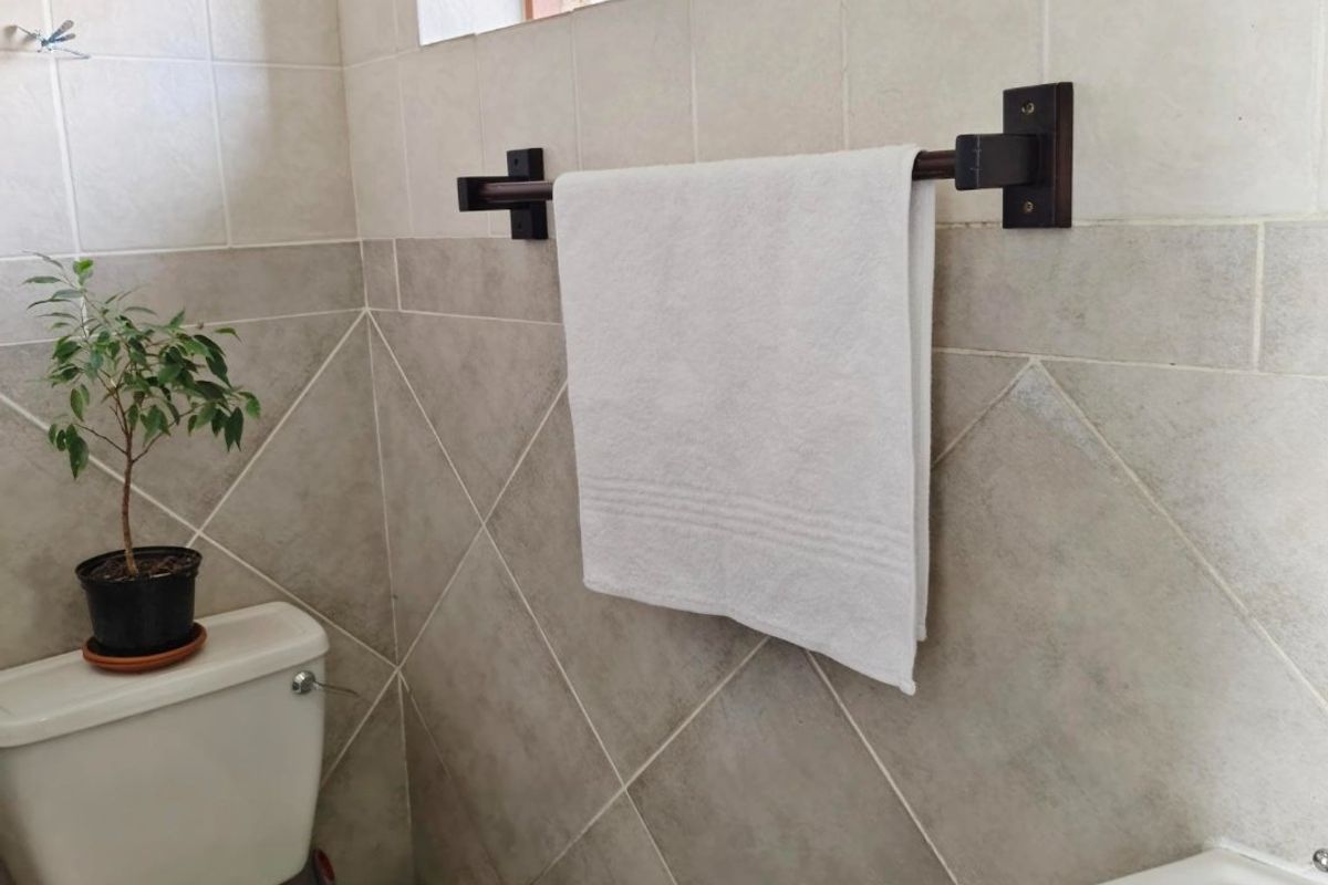 A compact bathroom featuring neutral ceramic wall and floor tiles, a pedestal basin, a standard toilet, and a functional top-hung window.