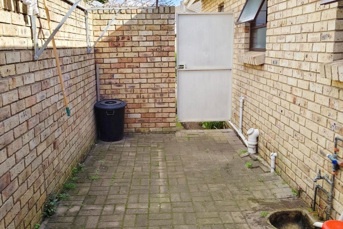 A functional rear courtyard area featuring brick paving, face brick walls, a wall-mounted washing line, and secure gated access.