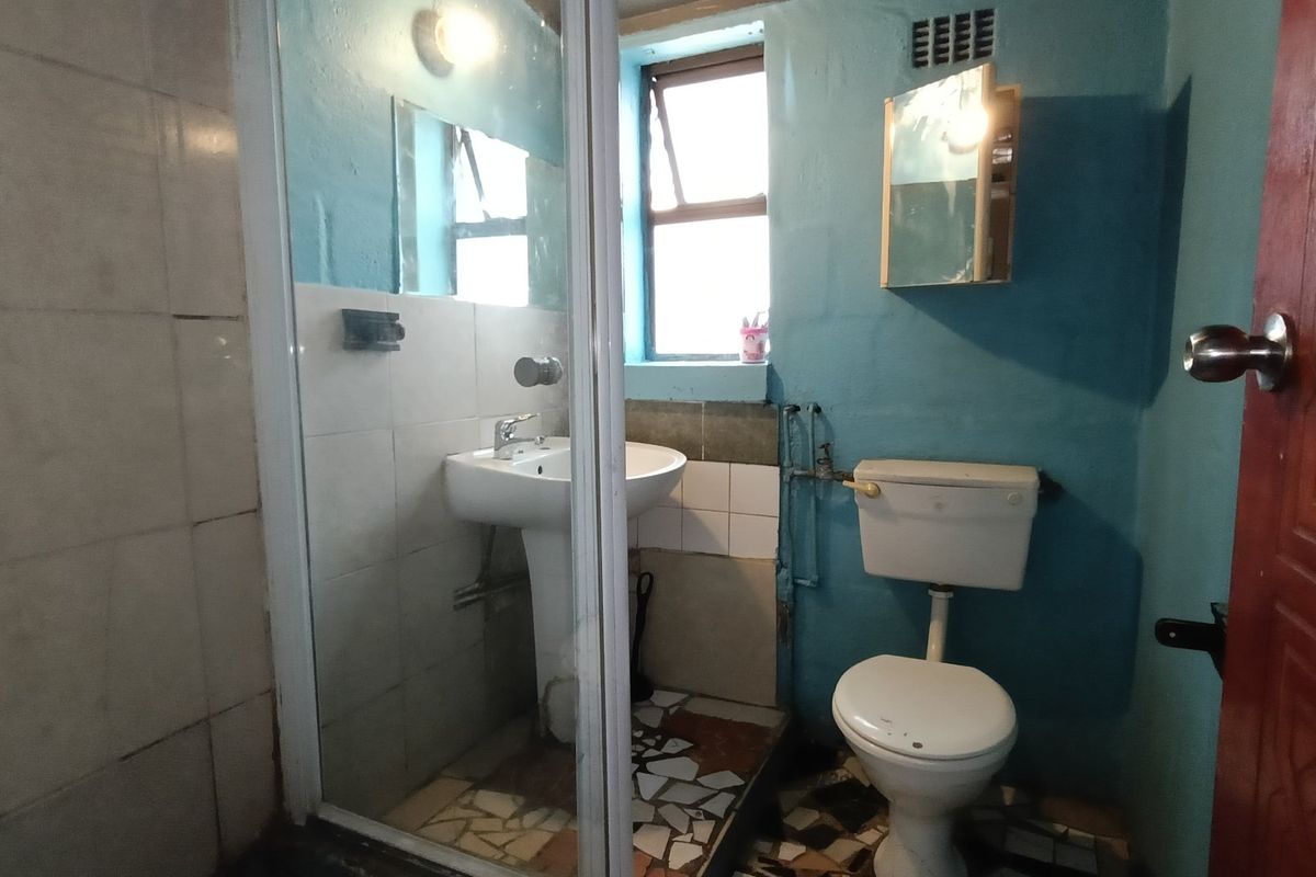 A compact bathroom featuring a pedestal basin, shower enclosure, and toilet, requiring cosmetic updates and repairs to finishes.
