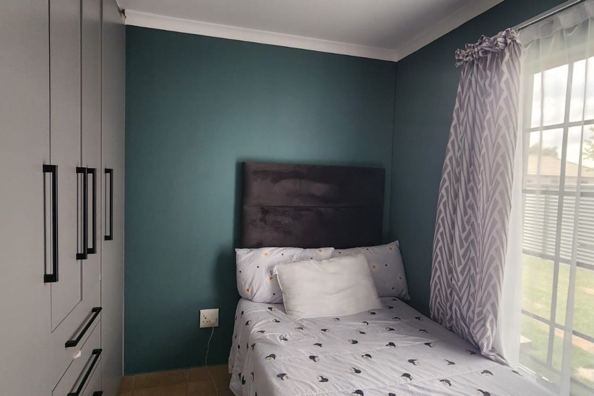 A well-maintained bedroom featuring built-in cupboards, tiled flooring, and a sliding glass door providing natural light and garden access.