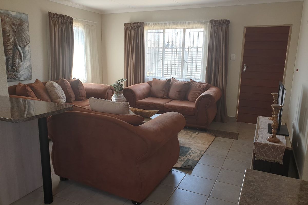 A comfortable living room featuring tiled flooring, large windows with security bars, and a solid timber door.