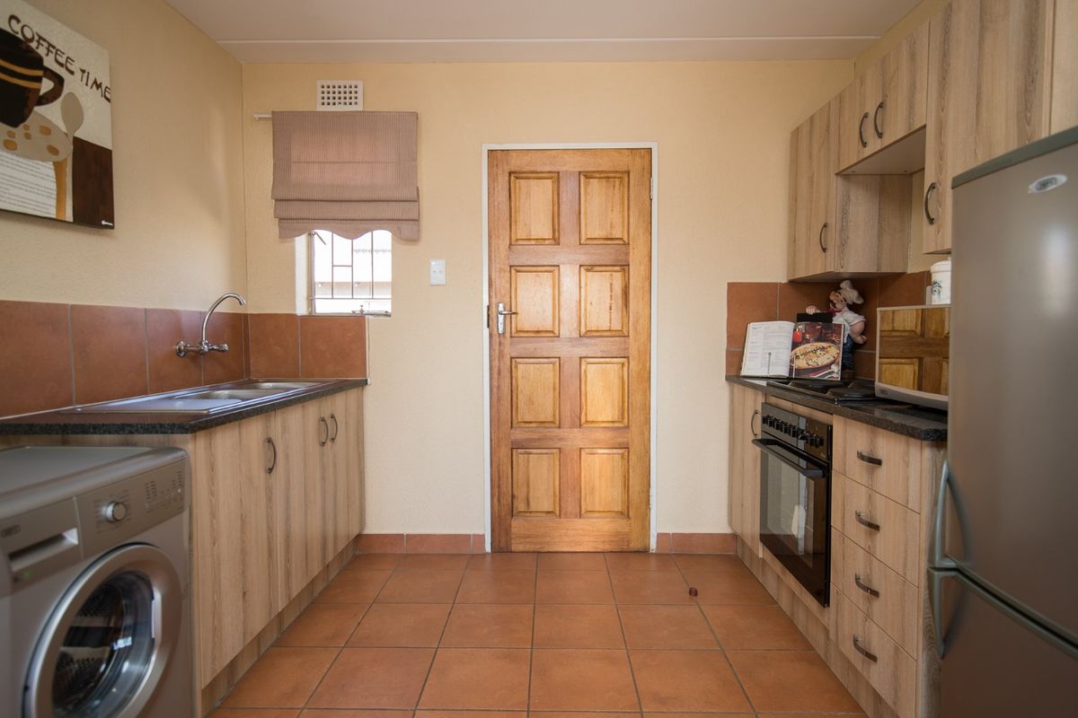 Functional kitchen featuring laminate cabinetry, granite countertops, tiled splashbacks, and built-in oven, with direct access to an exterior door.