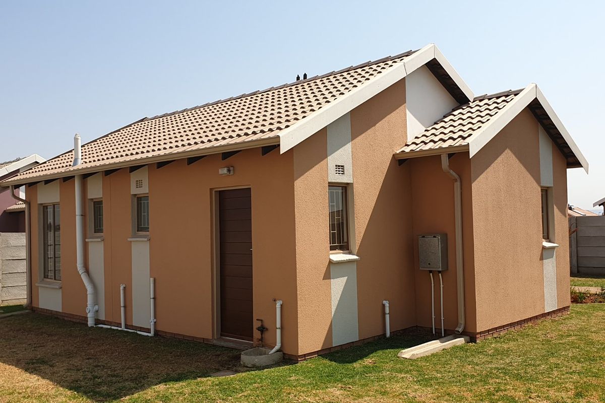 A well-maintained rear exterior view of a single-story house featuring a tiled roof, textured plaster finish, and secure window bars.