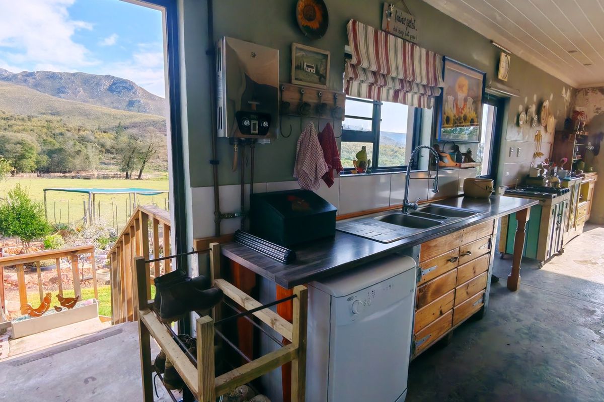 Rustic kitchen featuring wooden cabinetry, stainless steel sink, and gas geyser, with direct access to an outdoor deck and scenic mountain views.