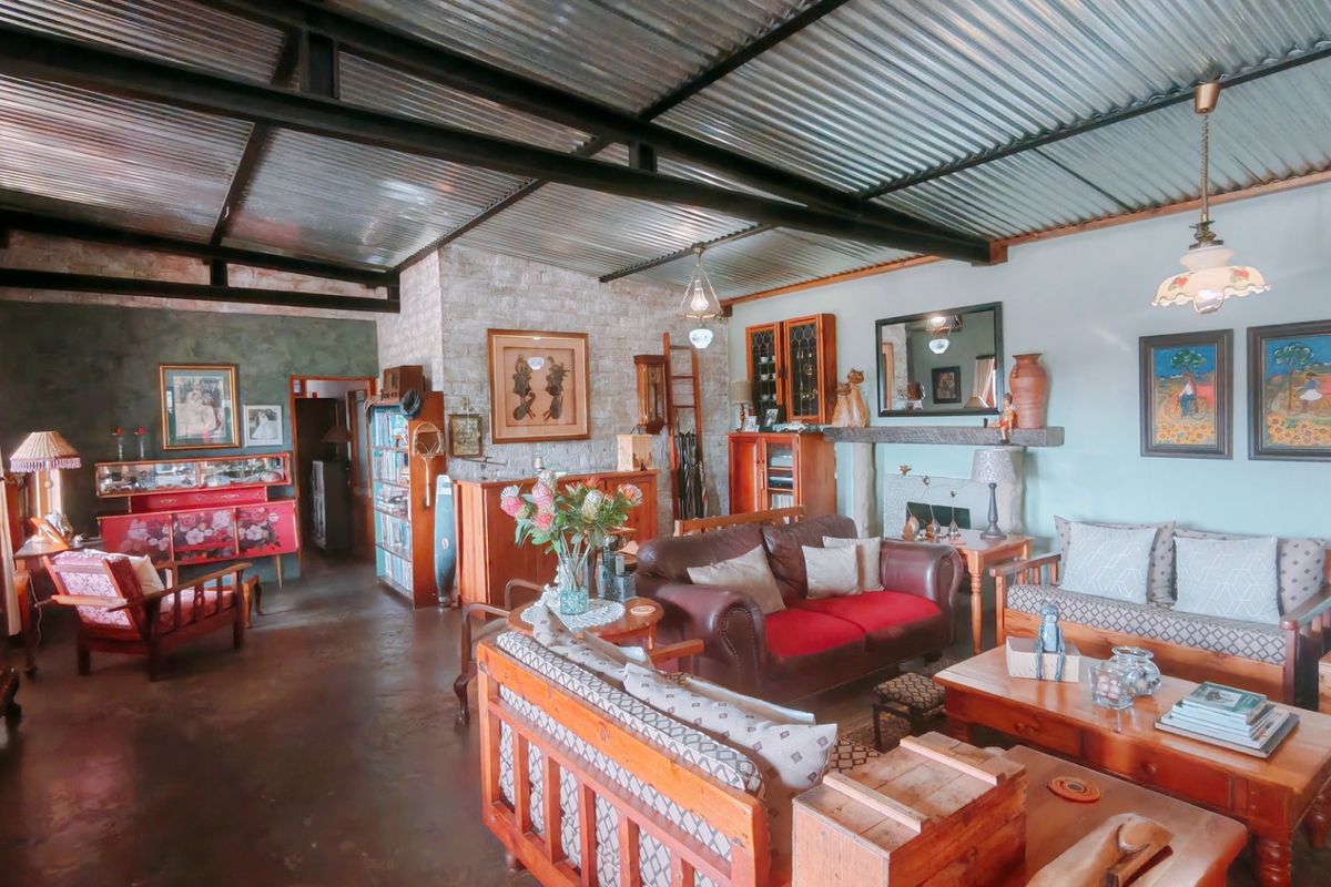 Spacious living area featuring a rustic corrugated metal ceiling, exposed steel beams, a stone feature wall with a fireplace, and polished concrete flooring.