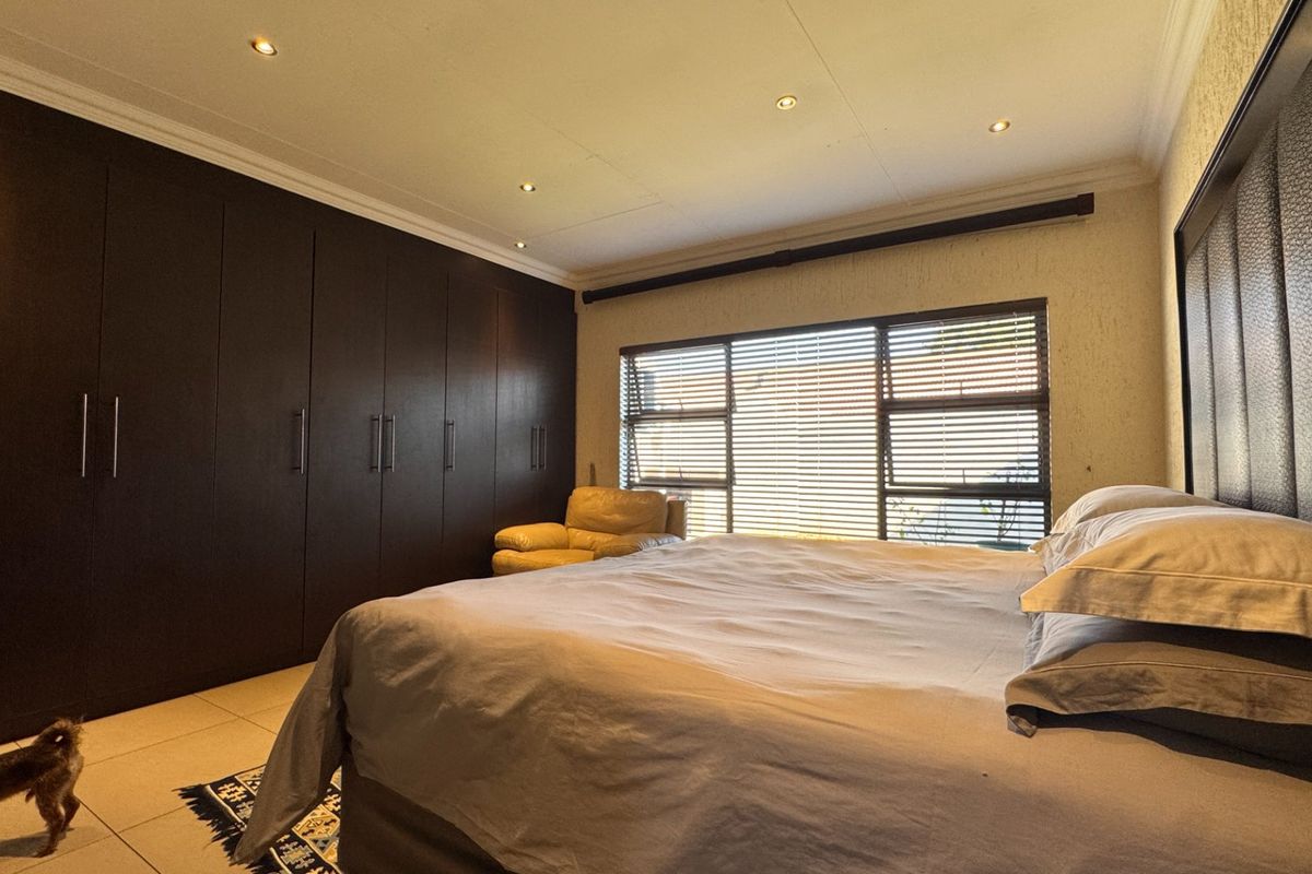 Spacious bedroom featuring extensive dark wood built-in cupboards, recessed downlighting, tiled floors, and large windows with fitted horizontal blinds.