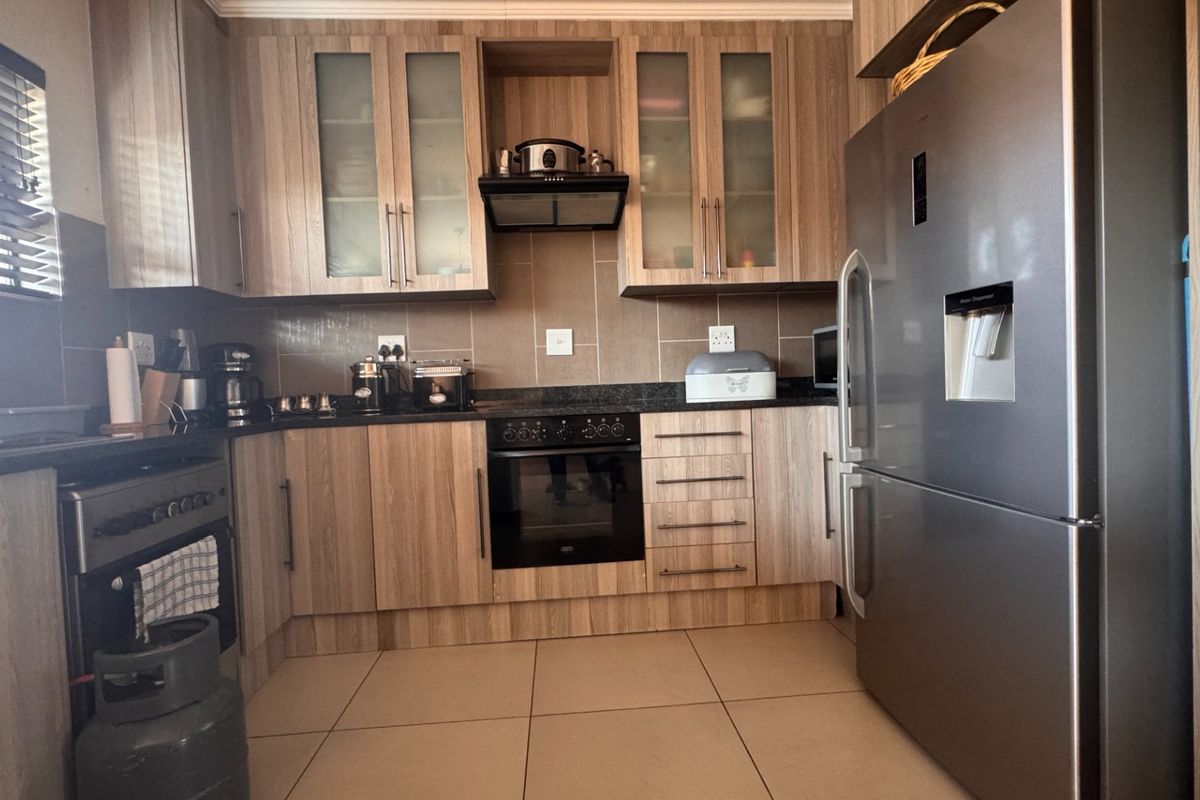 A functional kitchen featuring wood-look cabinetry, dark laminate countertops, a built-in oven with extractor fan, and neutral floor tiles.