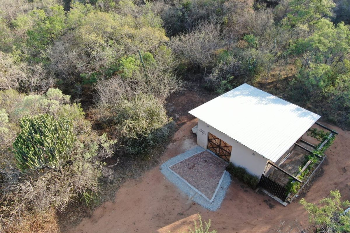 Aerial view of a detached building featuring a corrugated metal roof, paved entrance, and timber pergola, set within a natural bushveld environment.