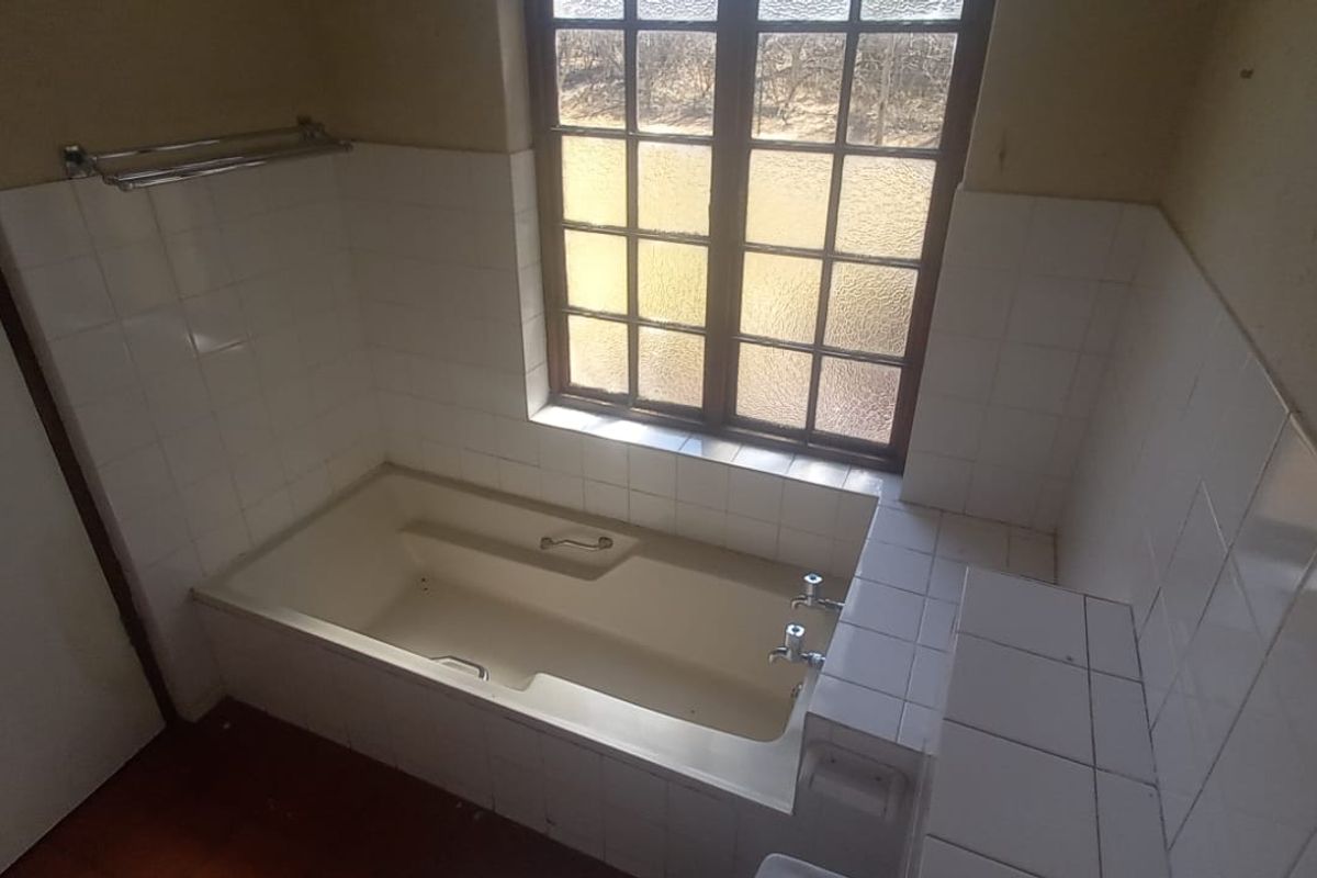 A dated bathroom featuring a built-in bathtub with tiled surround and a window, offering a blank canvas for renovation.