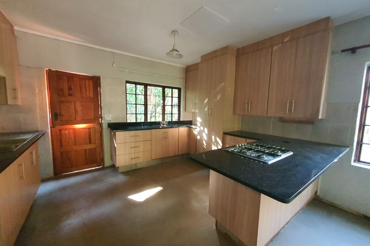 A functional kitchen featuring light wood cabinetry, dark granite countertops, a built-in gas hob, and direct access to the exterior.