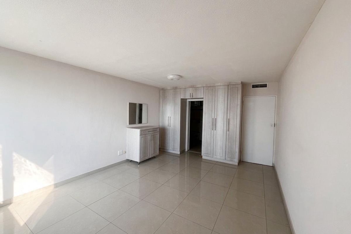 A bright bedroom featuring neutral tiled flooring and extensive built-in cupboard storage, offering a clean and functional living space.