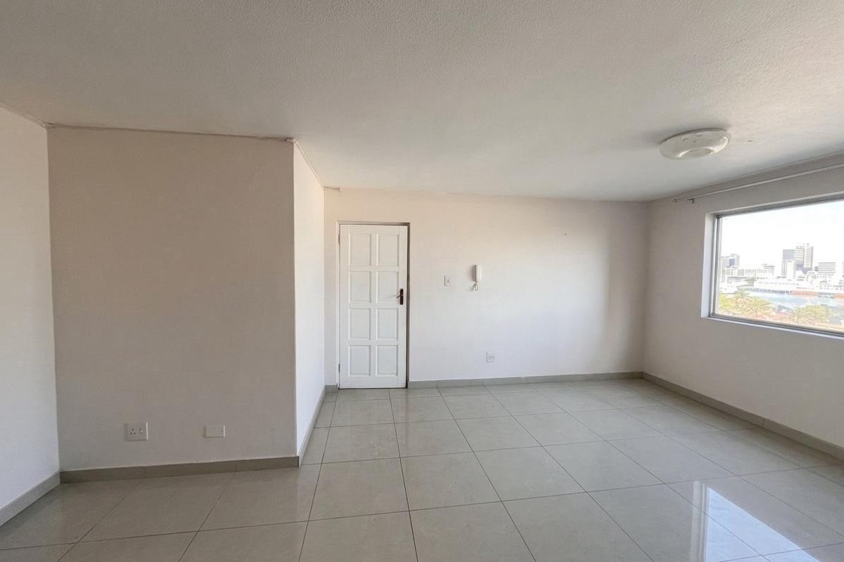 A bright, empty living area featuring neutral tiled flooring, a built-in intercom system, and large windows offering an urban view.