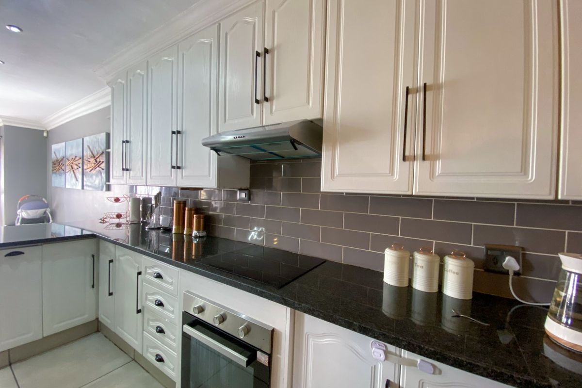 A well-maintained kitchen featuring white cabinetry, dark granite countertops, a subway tile backsplash, and integrated stainless steel appliances.
