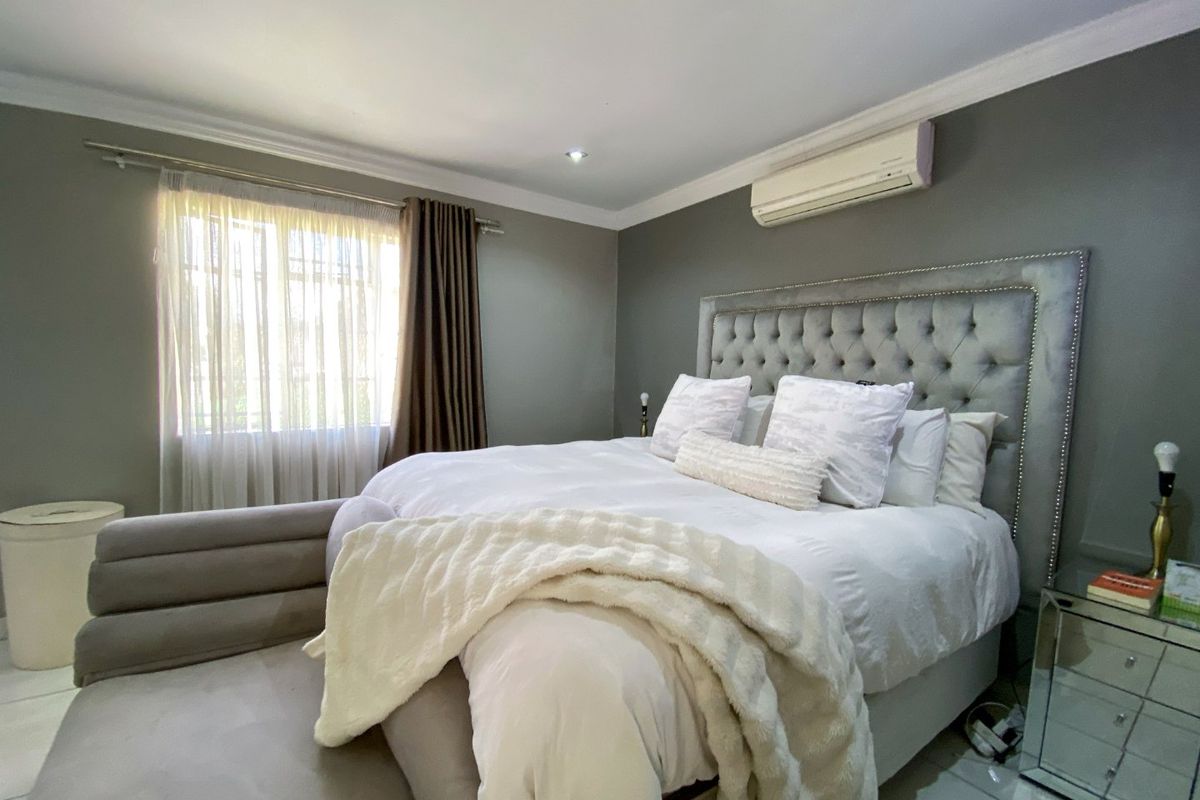 A well-maintained bedroom featuring tiled flooring, cove cornicing, and a wall-mounted air conditioning unit.