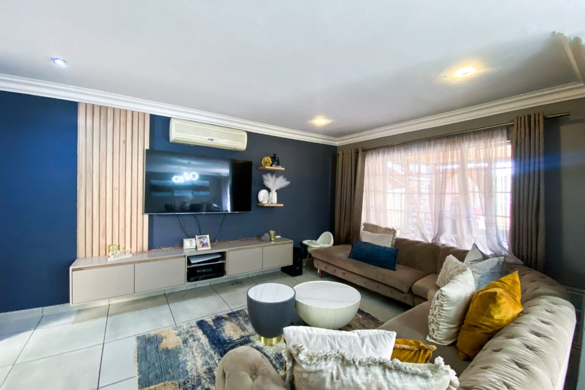Modern living room featuring a slatted timber accent wall, built-in media cabinetry, wall-mounted air conditioning, and large windows with neutral curtains.