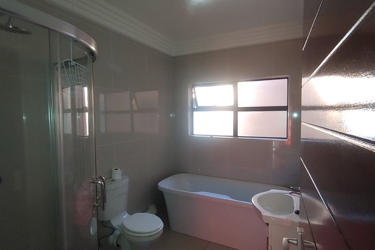 A modern bathroom featuring a glass shower enclosure, a freestanding bathtub, a vanity basin, and neutral wall and floor tiling.