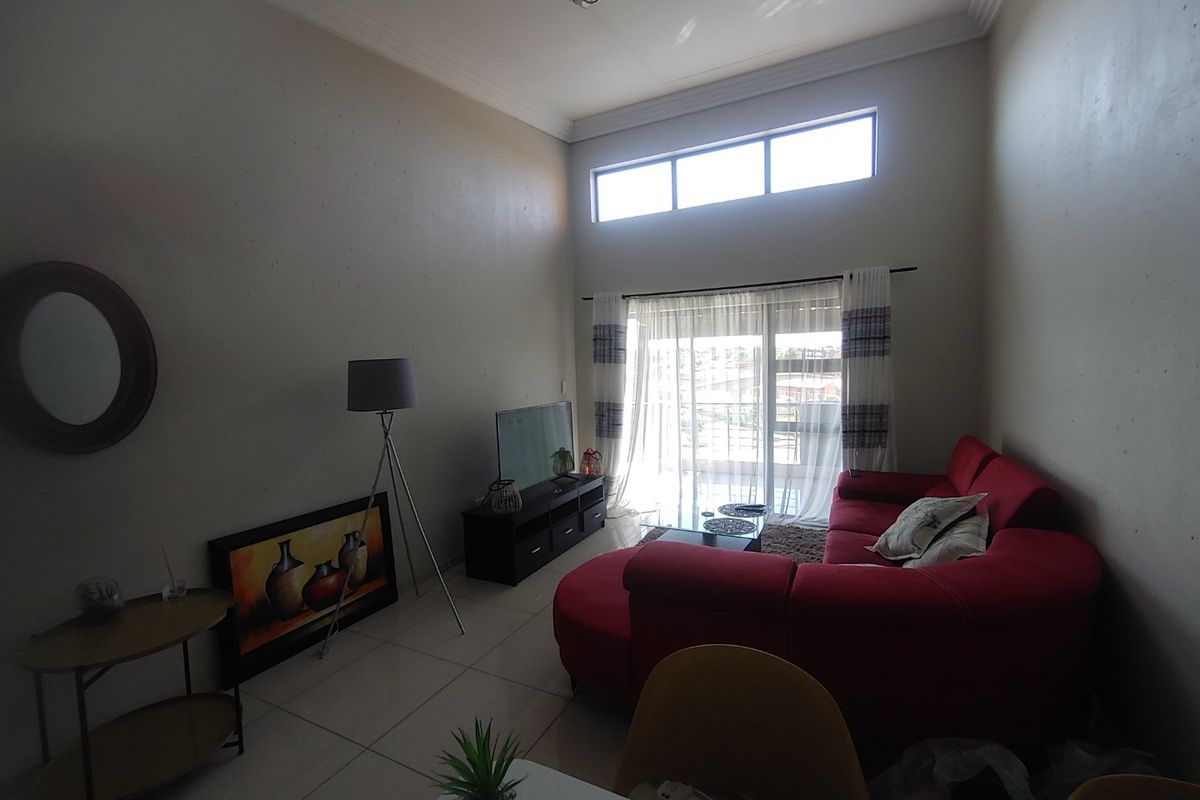 Spacious living room featuring high ceilings, tiled flooring, and large sliding glass doors leading to a balcony, providing ample natural light.