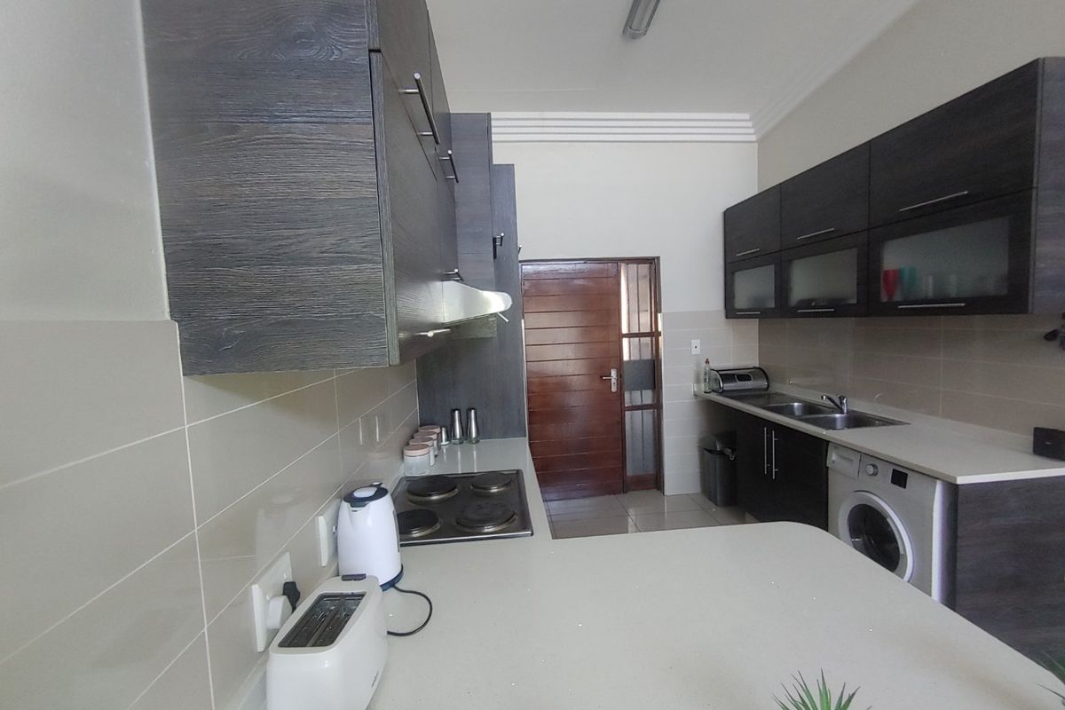 A functional kitchen featuring dark wood-look cabinetry, stone countertops, an electric hob, and an integrated washing machine with a tiled backsplash.