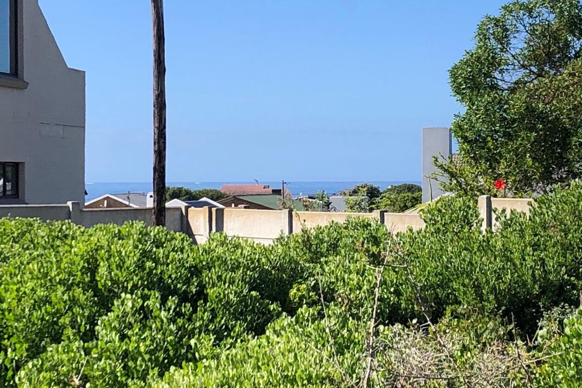 A view of the distant ocean horizon captured from the property, framed by surrounding residential structures and established garden vegetation.