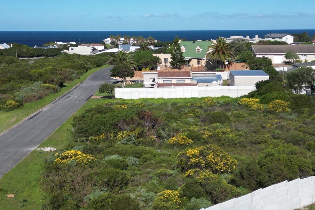 Aerial view of a vacant residential plot featuring coastal vegetation, adjacent to a paved road and bordered by a precast concrete wall.