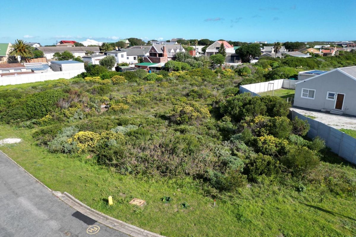 Aerial view of a vacant residential plot featuring natural vegetation, adjacent to established housing and a paved street.