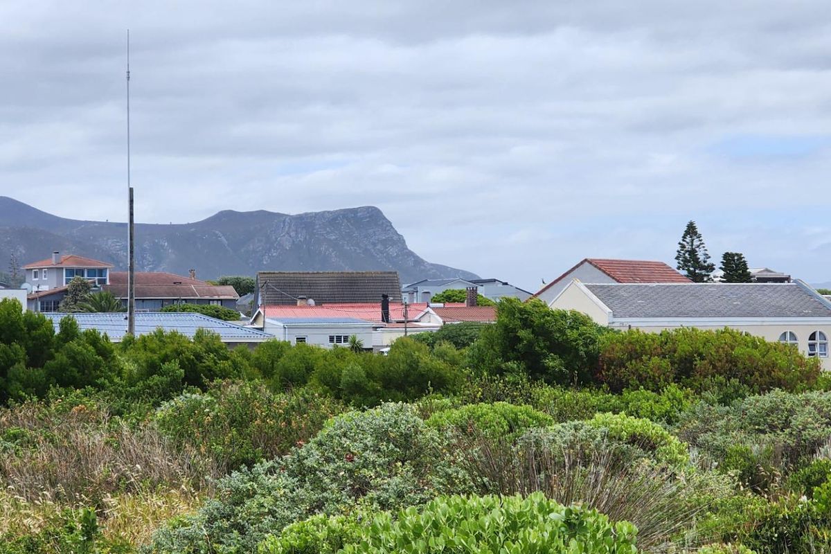 A scenic view overlooking a residential neighborhood with lush coastal vegetation in the foreground and mountain ranges in the distance.