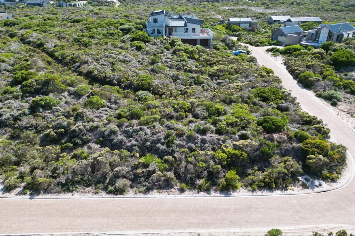 An aerial view of a vacant residential plot featuring natural coastal vegetation, adjacent to a paved road with established kerbing.