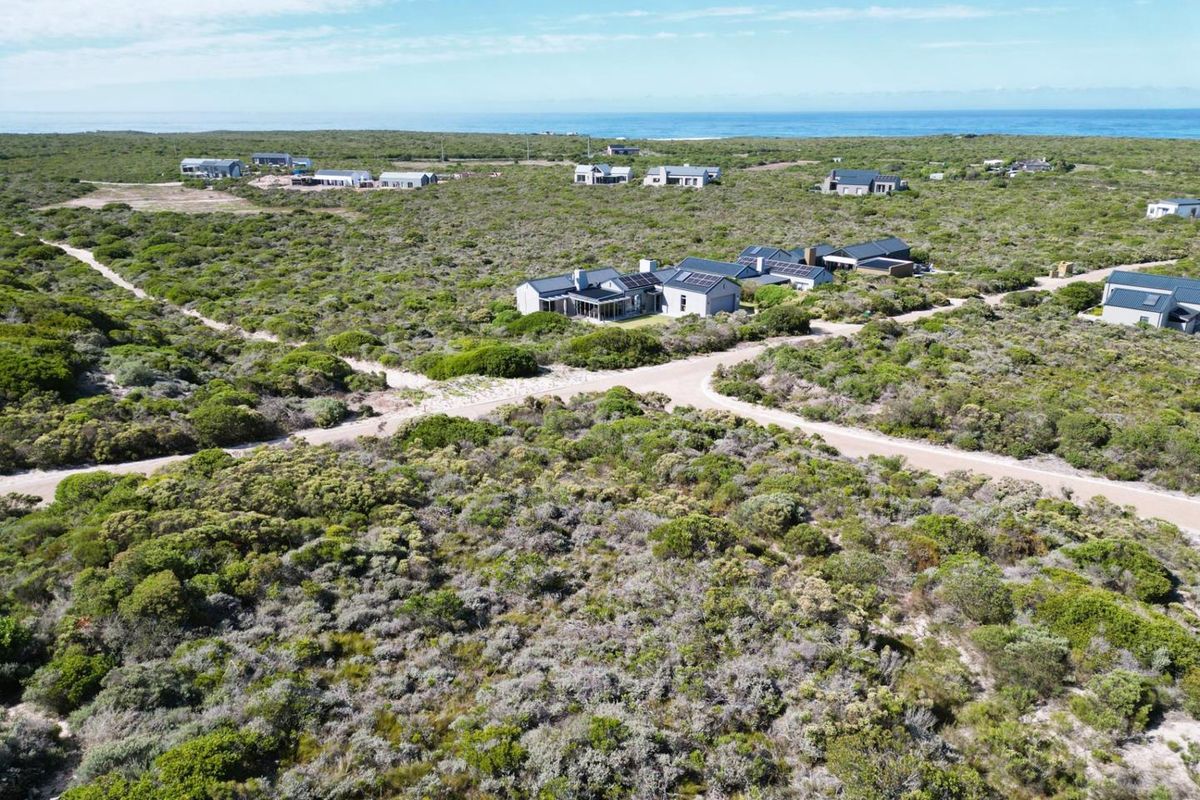 Aerial view of a residential estate featuring modern homes, gravel roads, and surrounding coastal landscape with ocean views.