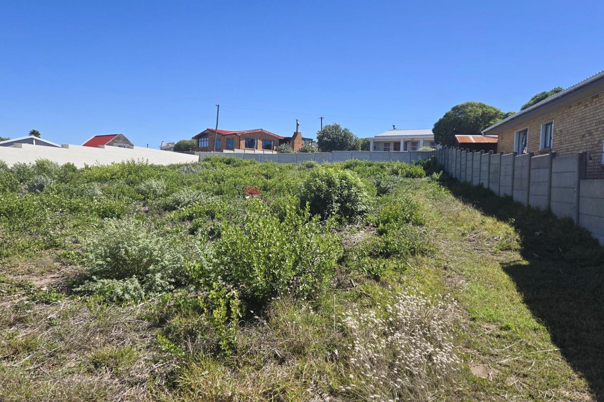 A vacant residential plot featuring natural vegetation and enclosed by precast concrete boundary walls on multiple sides.