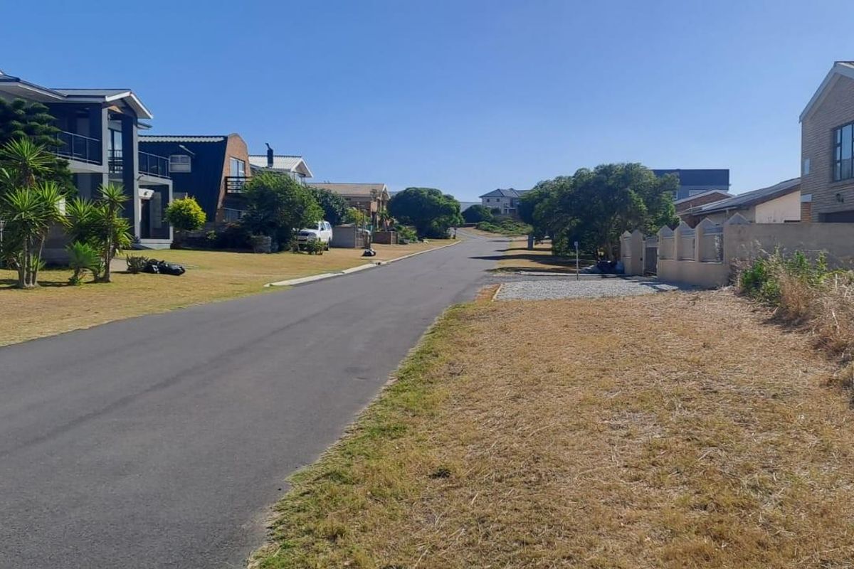 A view of the residential street showing the paved road, surrounding neighborhood homes, and the vacant plot frontage.